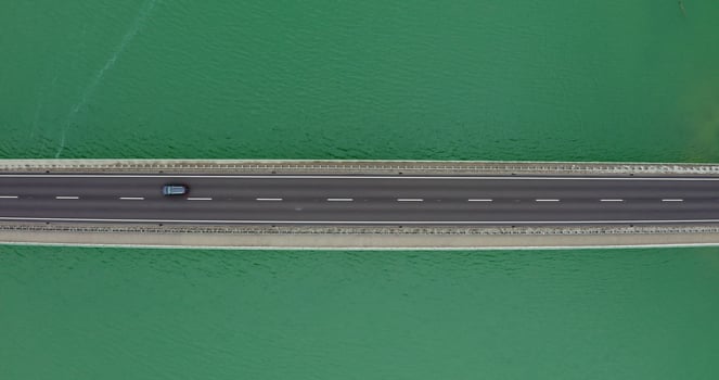 Narrow road bridge with cars passing over it, over a river with a shallow ripple of waves. recording from a drone photo