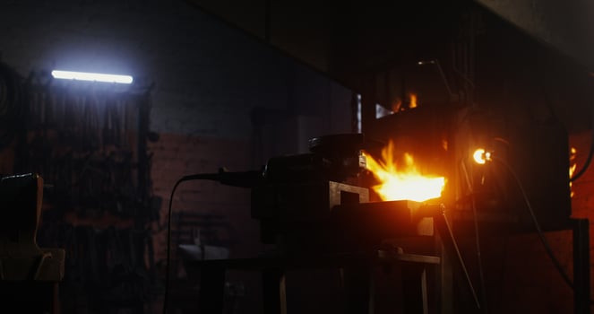 Blacksmith in protective gear and goggles takes an angle grinder and starts to cut off a part of a metal blank while working in a forge. 4k , red komodo photo