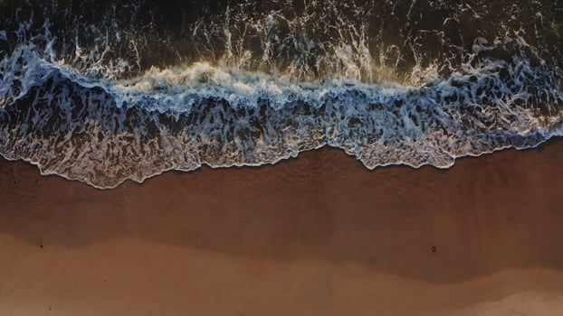 Top view from a drone on the coastline. Sea waves wash the sandy beach. Foamy water washes the sand in beautiful patterns, a bird's-eye view. No people. photo