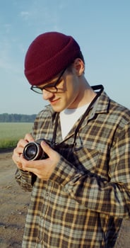 A young man takes photographs with a camera while standing on a gravel road photo