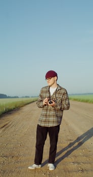 Male photographer takes photos while walking along a gravel road among agricultural fields on a sunny day. 4k vertical , red komodo