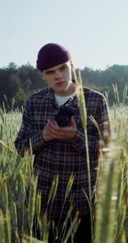 A man takes photos with a camera, standing between ears of wheat in an agricultural field on a summer sunny day. 4k vertical , red komodo