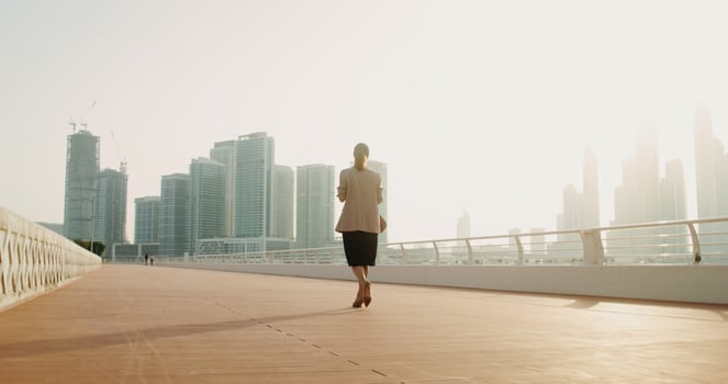 A woman in business clothes walking with a disposable cup in her hands walks along the embankment on a sunny day. Rear view photo