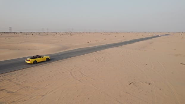 The drone flies over a yellow convertible driving along the road past the sand dunes of the desert photo