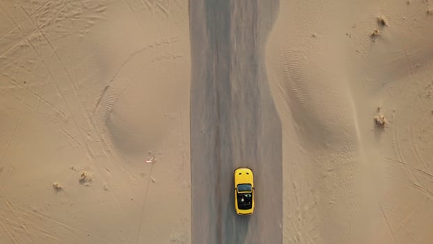 Top view of a yellow car driving on a road in the middle of the desert. The asphalt is covered with sand - middle photo