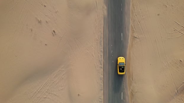 Top view of a yellow car driving on a road in the middle of the desert. The asphalt is covered with sand photo