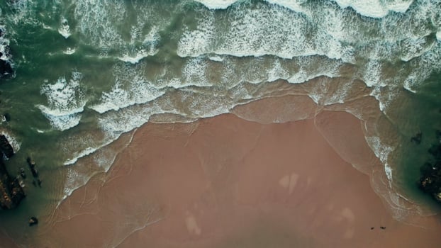 Drone rises above the seashore. A sandy beach between a stone reef. Sea waves are hitting the shore photo