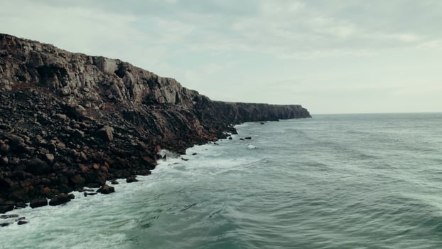 A rocky cliff on the seashore. The sea waves are beating against the rocks. Drone - against photo