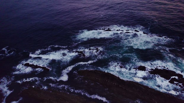 A bird's-eye view of the sea at sunset. Foam waves wash the stone reefs on the shore. Drone photo