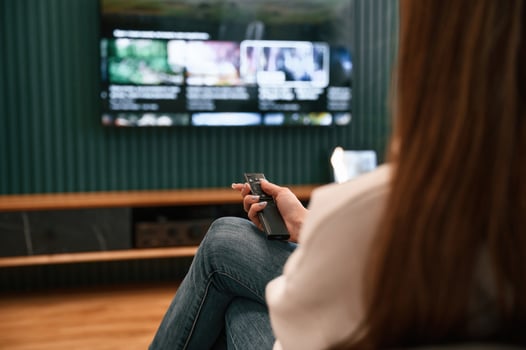 Woman is sitting at home watching TV,, holding remote controller photo