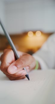 A child's hand is writing in a notebook, a girl is doing homework sitting at a table in the kitchen, close-up of her hand - writing photo