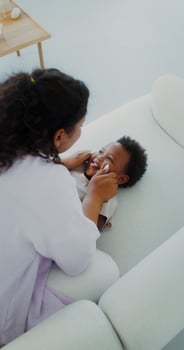 Mom and daughter of African-American appearance laugh and play together on the couch indoors, mom tickles the baby - tickles photo