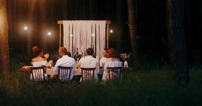 Guests smile and talk while sitting at a beautifully set festive table outdoors at night by candlelight - festive photo