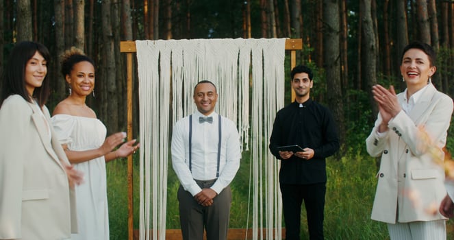 The bride walks to the altar passing by the applauding guests. The groom is waiting for her standing near the priest. They kiss when they meet. Wedding in the forest photo