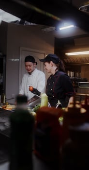 A man and a woman in a chef's uniform talk and smile while cooking in the restaurant kitchen together photo