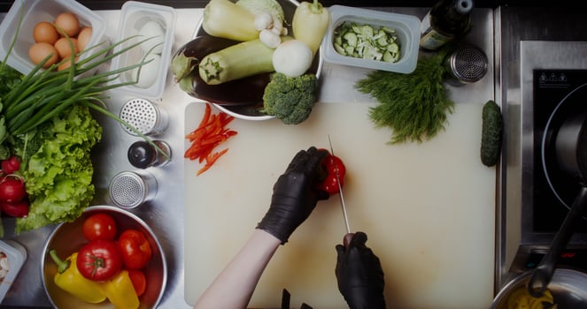 A woman in disposable black gloves cuts peppers standing near a table full of vegetables, close-up of her hands, top view - peppers photo