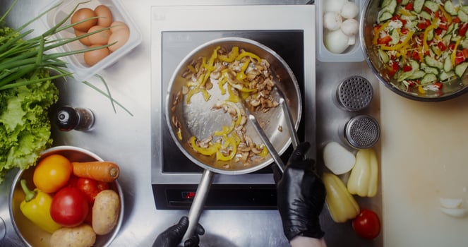 A woman in disposable black gloves adds spices to mushrooms with pepper in a frying pan and mixes everything with tongs, top view, close-up of her hands photo