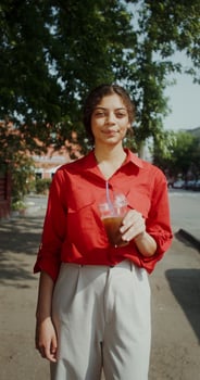 A young woman in casual clothes smiles, and looks at the camera drunk lemonade from a disposable cup with a straw standing on a city street photo