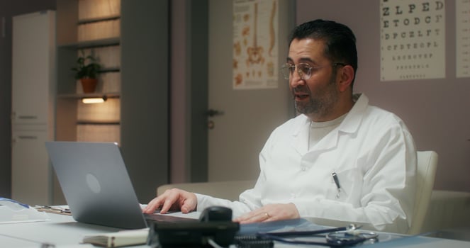 The doctor is talking on a chat on a laptop sitting at a table in the medical office at the clinic - medical photo