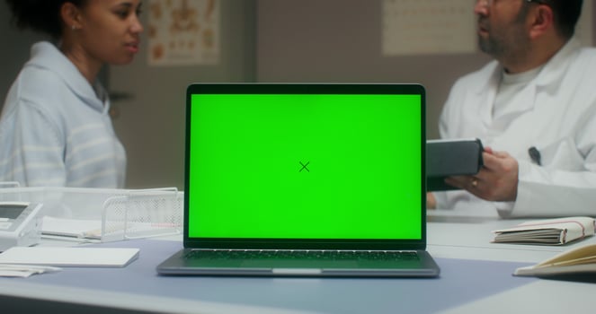 A laptop with a green screen is on the table in the medical office. A doctor is talking to a female patient photo