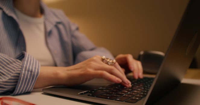 A woman typing on a laptop keyboard sitting at a table indoors, close-up of her hand, unrecognizable person photo