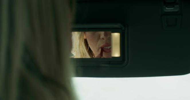 A stylish woman paints her lips sitting in the driver's seat in a car and looking in the mirror, close-up of her reflection photo