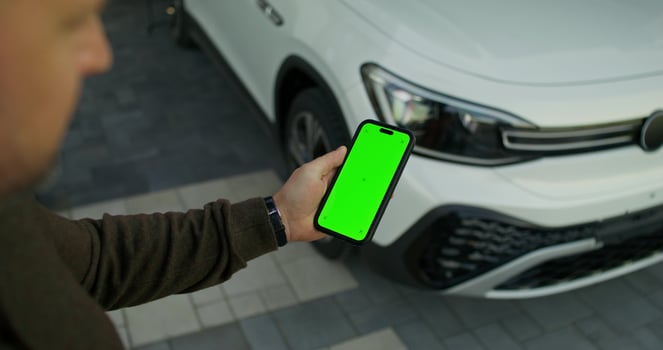 A man holds a mobile phone with green screen in his hand, standing near an electric car. He opens the car with his phone. Close-up of his hands. photo