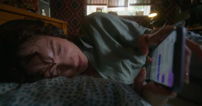 A woman with headphones on her head uses a mobile phone lying in bed at home, she smiles photo