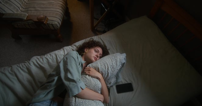 A woman is crying and hugging a pillow lying in bed at home. The mascara is smeared under the eyes. The mobile phone is on her bed photo