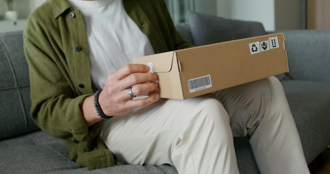 A man in casual clothes opens a box sitting on the couch. Online shopping with home delivery. Daylight - Online photo