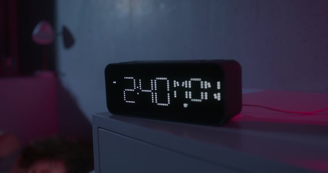A woman uses a mobile phone lying on the bed. Dark room, home interior. The electronic clock is on the bedside table - mobile photo