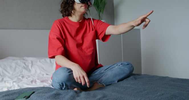A woman wearing a red shirt and glasses sitting on a bed photo