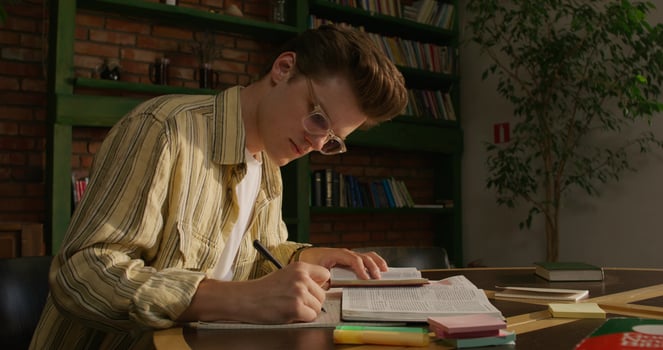 A young man is sitting at a table with a book and pen photo
