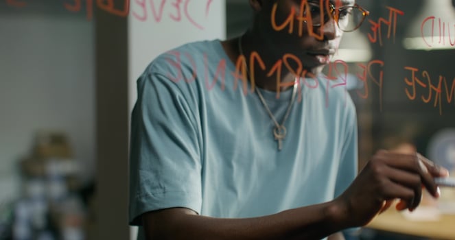 A man in casual clothes uses a tablet and writes on a glass writing board in the office. Daylight - tablet photo