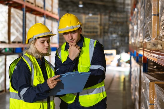 Two workers in safety gear looking at a clipboard photo