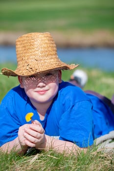 A portrait of a boy in a straw hat lies on a summer meadow with a dandelion. photo