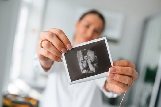 Standing, and smiling. Woman in ,white coat is holding ultrasound picture of baby photo