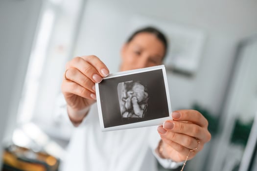 Standing and smiling., Woman in white coat is holding ultrasound picture of baby photo