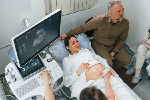 Man is sitting with his wife. Pregnant woman is lying down in the hospital, doctor does ultrasound photo
