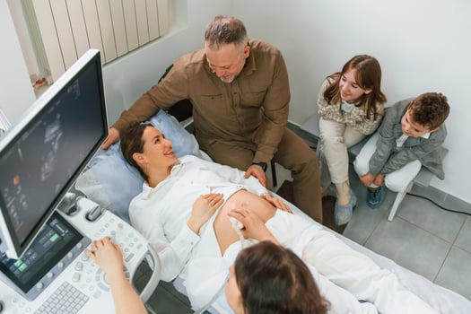 Top view. Kids, and, husband supporting. Pregnant woman is lying down in the hospital, doctor does ultrasound photo