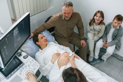 Top view.. Kids ,and ,husband supporting. Pregnant woman is lying down in the hospital, doctor does ultrasound photo