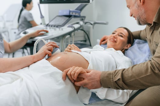 Happy ,husband, is sitting and supporting his wife. Pregnant woman is lying down in the hospital, doctor does ultrasound photo