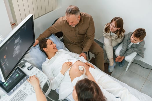 Top view.. Kids ,and husband supporting. Pregnant woman is lying down in the hospital, doctor does ultrasound photo