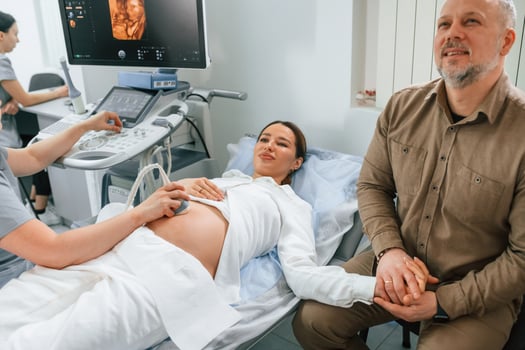 Man, is sitting with his wife. Pregnant woman is lying down in the hospital, doctor does ultrasound photo