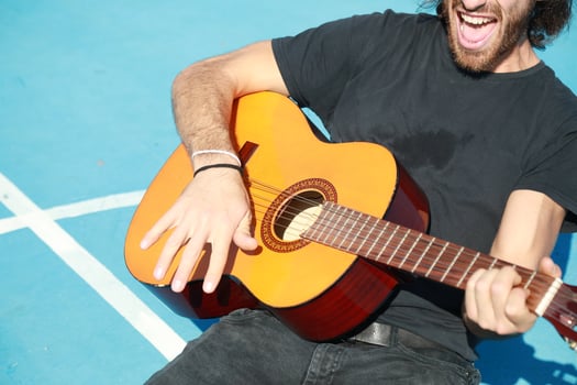 Outdoor Long Hair Man Plays Classical Guitar Unleashed Outside In Blue Field photo