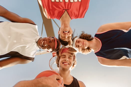 Group of happy basketball players putting their heads together in unity outdoors, bottom view. Cheerful young sportsmen getting primed for game. Team work in sports concept photo