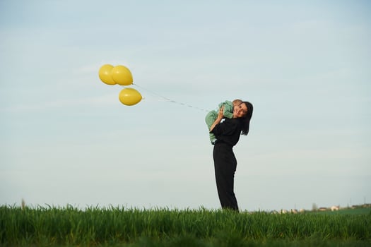 With, yellow colored balloons.. Mother with her little baby son is outdoors on the agricultural field photo