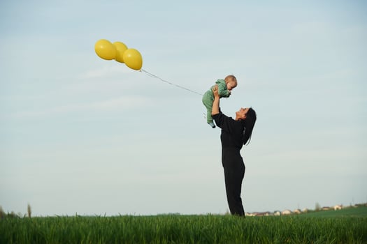 With yellow colored balloons., Mother with her little baby son is outdoors on the agricultural field photo