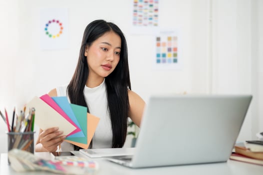 Asian woman is working on the design in laptop with selected colors from paper color charts. photo