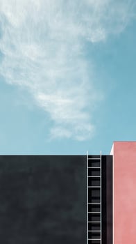 A striking architectural setup displays a black wall adjacent to a pink structure, complemented by a blue sky and wispy clouds above photo
